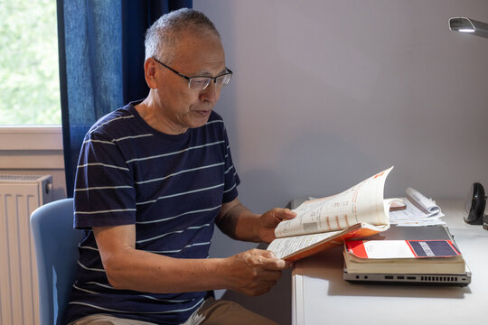 retired senior man in glasses learning new language, reading book