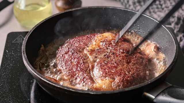 A chef cooks a beef steak on a pan in the kitchen and turns it to the other side, close-up. Process of making delicious steak.