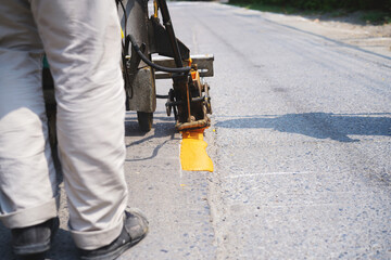 Man use thermoplastic road marking paint machine, hot melt marking paint machinery spraying a yellow line on concrete road.