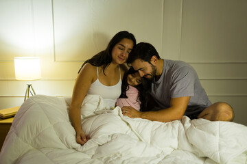 Heartwarming scene of a family cuddled together in bed at night, basking in the peaceful glow of a bedside lamp