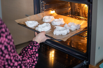 A person in a patterned shirt slides a tray of pavlova, meringues into the oven, an intimate moment...