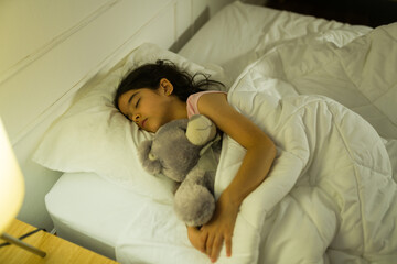 Serene hispanic little girl deeply asleep, embracing a plush toy in her cozy bedroom at night under soft lighting