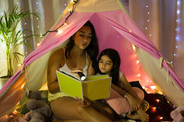 Mother and daughter bonding over a story in a cozy bedroom tent on a peaceful evening at home