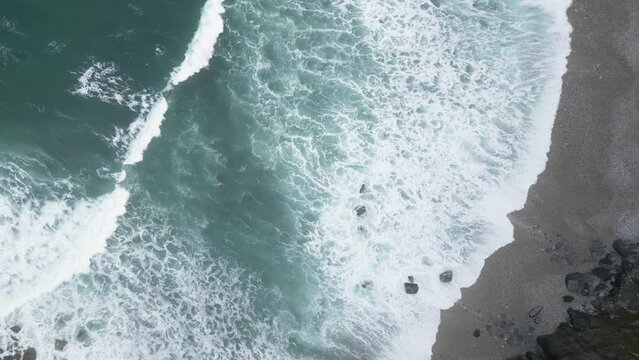 Aerial drone shot of sea waves crashing on sandy beach