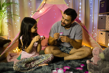 Dad and daughter have a fun tea party in a diy tent with fairy lights at night