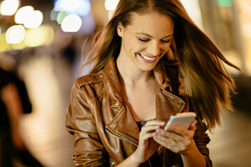 Young woman using smartphone downtown in the city at night