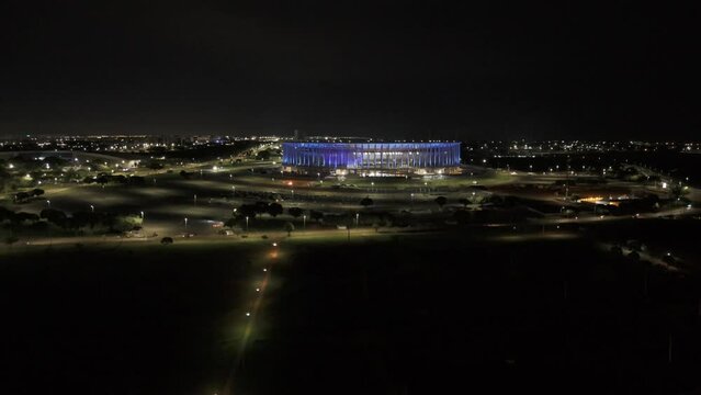Drone slowly rises in ultra wide shot of Arena BRB Mane Garrincha in blue light at night in Brasilia, Brazil