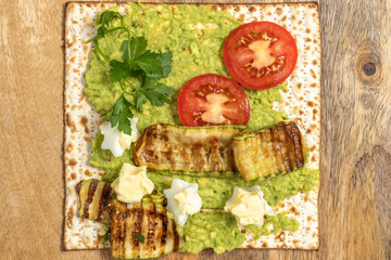Matzah toast with creamy avocado, fresh tomatoes, boiled eggs for Jewish holiday Pesach (Passover) on wooden background.