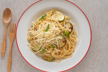 Spaghetti with grilled zucchini, parmesan cheese, spices on ceramic plate over cotton fabric background.