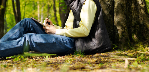 a man draws with a simple pencil in an album in the forest, sunny day spring summer, hobby, art