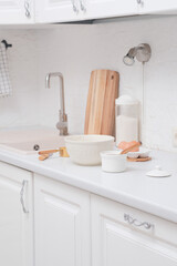 Home kitchen interior.Bowl with dough and spatula, eggs and bowl of sugar, napkin, knife on kitchen table in modern kitchen.