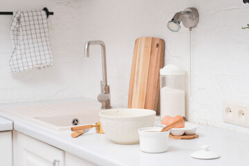Home kitchen interior.Bowl with dough and spatula, eggs and bowl of sugar, napkin, knife on kitchen table in modern kitchen.