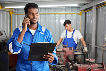 worker or technician talking on smartphone with customer and holding a clipboard in the factory