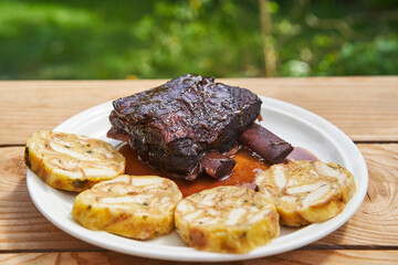 Slowly roasted beef ribs in the red wine and served with carlsbader bread dumplings on the white porcelain plate outside in the garden. Juicy, tasty and tender dish from cuisine of Czech Republic.
