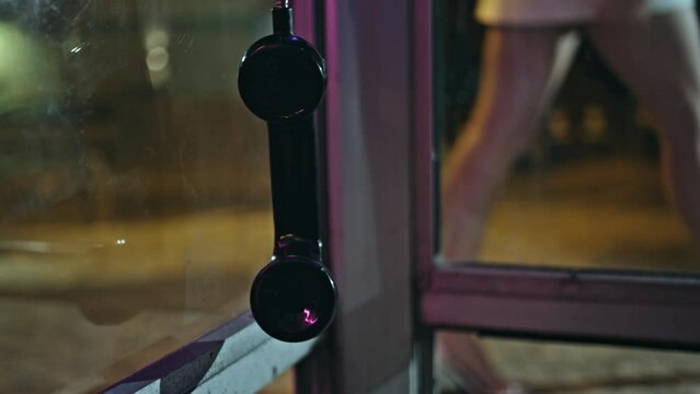 Broken payphone swinging wire at blurred evening city closeup. Telephone hanging