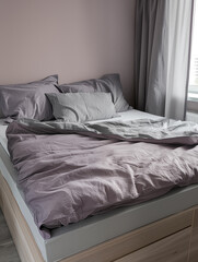 Bed with lavender and gray bedding linen in modern bedroom with natural light from window