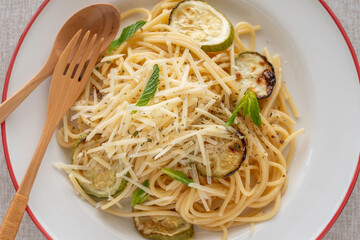 Spaghetti with grilled zucchini and parmesan cheese on ceramic plate over cotton fabric background.