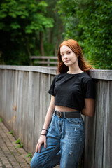 Red haired twelve year old girl with freckles posing leaning against a fence, Belgium