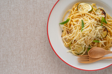 Spaghetti with grilled zucchini, parmesan cheese, spices on ceramic plate over cotton fabric background.