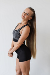 Young female athlete stands confidently in studio, showcasing her fitness attire. Confident female serene expression and detailed sporty hairstyle, which complements her toned physique.