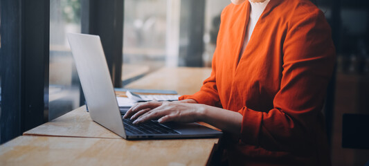 Asian Business woman using calculator and laptop for doing math finance on an office desk, tax, report, accounting, statistics, and analytical research concept