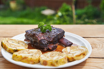 Traditional recipe from cuisine of Czech Republic. Slowly roasted beef ribs in the red wine and served outside on white plate in garden restaurant with carlsbader style bread dumplings as a side dish.