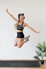 Energetic female athlete showcasing joyful high jump in minimalist fitness studio. Dressed in stylish sportswear dynamic movement and positive demeanor communicate health, well-being, and vitality.