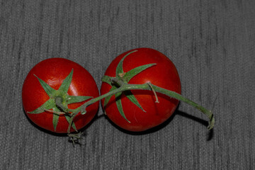 Two fresh red tomatoes with stem still attached on a grey background