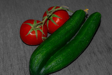 two fresh red tomatoes with stem still attached and two fused cucumbers on a grey background