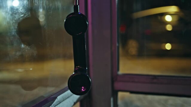Hanging public telephone night closeup. Black broken payphone swinging in air