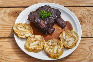 Top view on delicious and tender slowly roasted beef short ribs in red wine and vegetables and served on white porcelain plate with Czech style carlsbader bread dumplings. Traditional european dish.