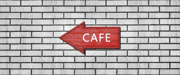 Red wooden arrow sign with the inscription CAFE hanging on a white brick wall. Left arrow pointer