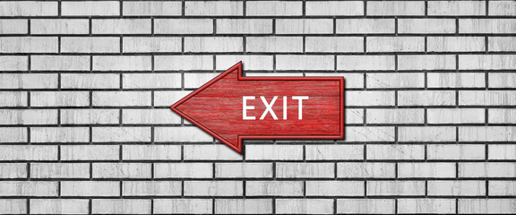 Red wooden arrow sign with the inscription EXIT hanging on a white brick wall. Left arrow pointer