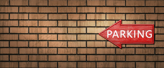 Fototapeta premium Red wooden shooter sign with the inscription PARKING hangs on a dark brick wall. Left arrow pointer