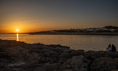 Spectacular sunset from Biniancolla cove, on the island of Menorca. Silhouette of two girls enjoying it, Spain