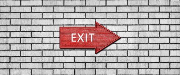 Red wooden arrow sign with the inscription EXIT hanging on a white brick wall. Right arrow pointer