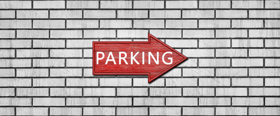 Fototapeta premium Red wooden arrow sign with the inscription PARKING hanging on a white brick wall. Right arrow pointer