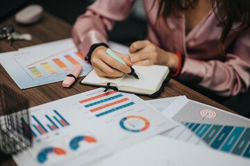 A professional woman in a pink blouse meticulously reviews and annotates financial charts and...