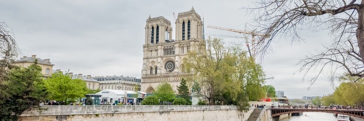 Panoramic view of the iconic Notre-Dame Cathedral in Paris on a cloudy day, with surrounding spring...