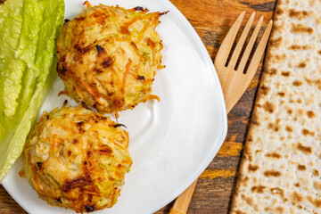Chicken Vegetables Cutlets served with lettuce leaf, wooden cutlery, matzah piece on ceramic plate for Jewish holiday Pesach.