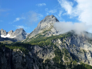 A picturesque view of the rocky mountain slopes covered with green forests. Above them is a blue sky