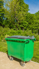 Green waste container on wheels in a sunny park, symbolizing urban recycling and environmental conservation efforts Related to: Earth Day, World Environment Day