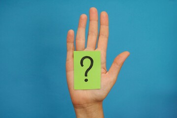 A green paper note with a question mark on it in a woman palm.
