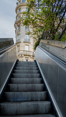 Ascending outdoor escalator leading to a classic European-style building, illustrating urban...