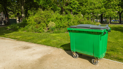 Large green waste container in a lush park on a sunny day, symbolizing environmental sustainability and waste management practices