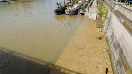 Flooded river promenade with partially submerged benches and tree shadows, indicating climate...