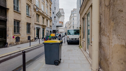 Quaint European city street with waste bins, bicycles, and parked vehicles, exemplifying urban life...