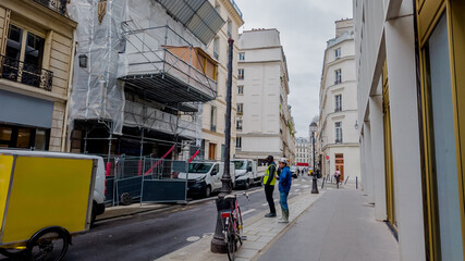 Urban European street scene with buildings under renovation, pedestrians, and parked vehicles on a...