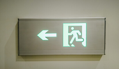 Illuminated green exit sign with running figure and arrow indicating direction, concept related to...