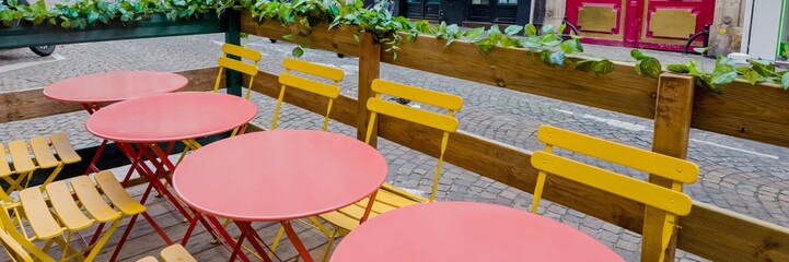 Colorful outdoor cafe setting with red tables and yellow chairs on a cobblestone street, ideal for...